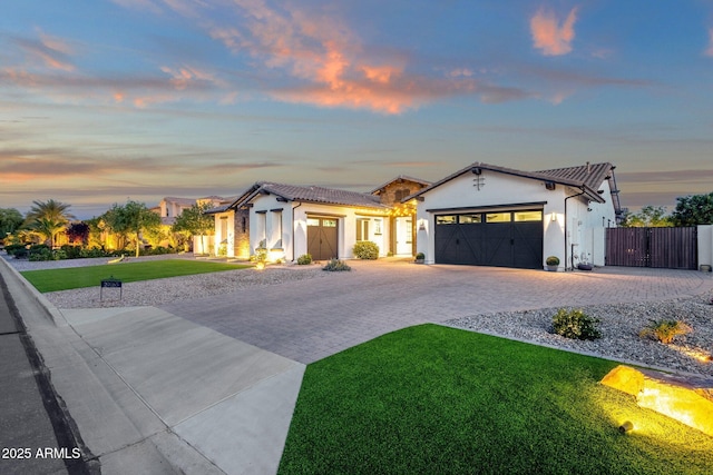 view of front of house with an attached garage, stucco siding, a front yard, a gate, and decorative driveway
