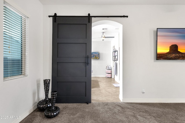 foyer with arched walkways, baseboards, light colored carpet, and a barn door