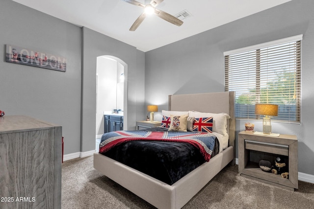 carpeted bedroom with ceiling fan, visible vents, arched walkways, baseboards, and ensuite bath