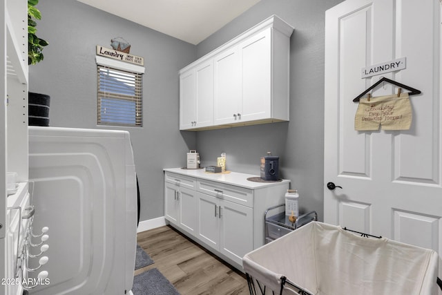 laundry room with baseboards, cabinet space, light wood-type flooring, and washer / clothes dryer
