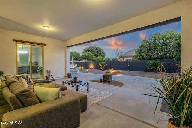 patio terrace at dusk featuring a fenced backyard and an outdoor living space with a fire pit