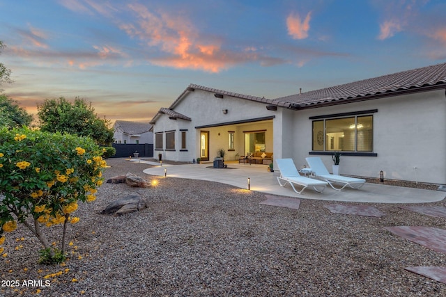 back of house at dusk featuring a patio area, stucco siding, a tile roof, and fence