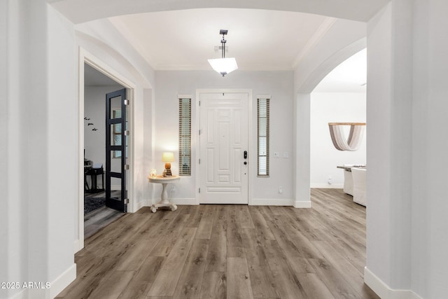entryway featuring crown molding, wood finished floors, baseboards, arched walkways, and a wealth of natural light