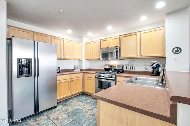 kitchen with stainless steel appliances, recessed lighting, light brown cabinetry, stone finish floor, and a sink