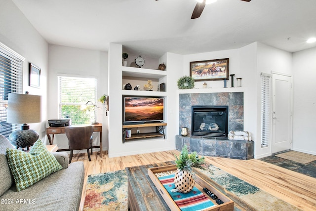 living room with wood finished floors, a tile fireplace, a ceiling fan, and baseboards