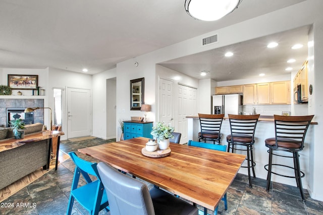 dining area featuring visible vents, stone finish floor, a tiled fireplace, and recessed lighting