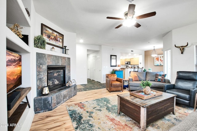 living area with baseboards, a fireplace, a ceiling fan, and wood finished floors