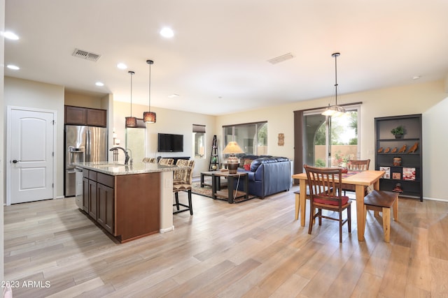 kitchen featuring hanging light fixtures, light stone counters, dark brown cabinetry, a center island with sink, and light hardwood / wood-style flooring