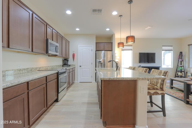 kitchen featuring appliances with stainless steel finishes, decorative light fixtures, an island with sink, a kitchen bar, and light hardwood / wood-style floors