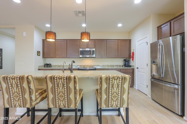 kitchen featuring decorative light fixtures, a breakfast bar area, light stone counters, stainless steel appliances, and light wood-type flooring