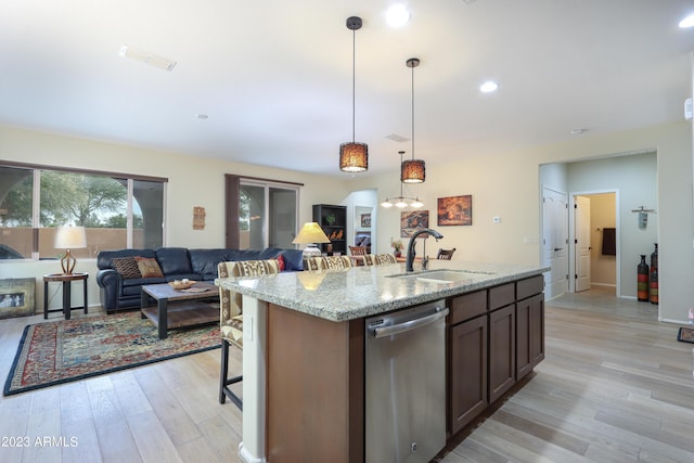 kitchen with sink, hanging light fixtures, a kitchen island with sink, stainless steel dishwasher, and light stone countertops