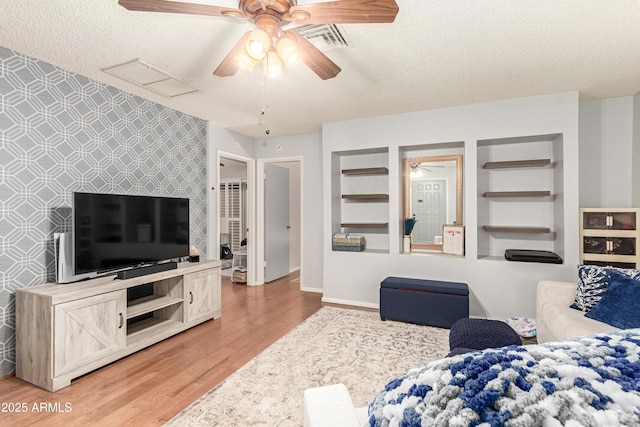 living room with ceiling fan, hardwood / wood-style flooring, built in shelves, and a textured ceiling