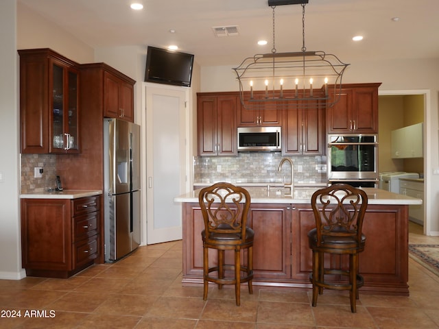 kitchen with pendant lighting, backsplash, tile patterned flooring, an island with sink, and appliances with stainless steel finishes