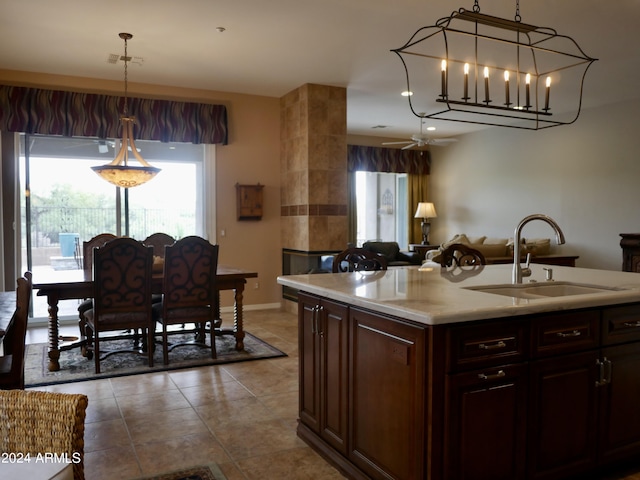 kitchen with dark brown cabinetry, a kitchen island with sink, sink, and pendant lighting