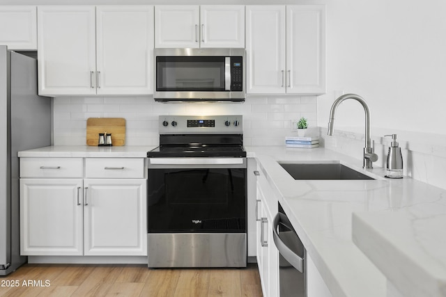 kitchen featuring light stone countertops, sink, stainless steel appliances, backsplash, and white cabinets