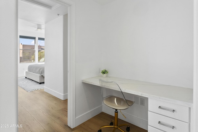 home office with light wood-type flooring, built in desk, and ceiling fan