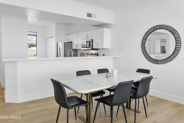 dining space featuring light hardwood / wood-style floors, ornamental molding, and sink