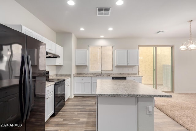 kitchen with white cabinetry, hanging light fixtures, a kitchen island, and black appliances