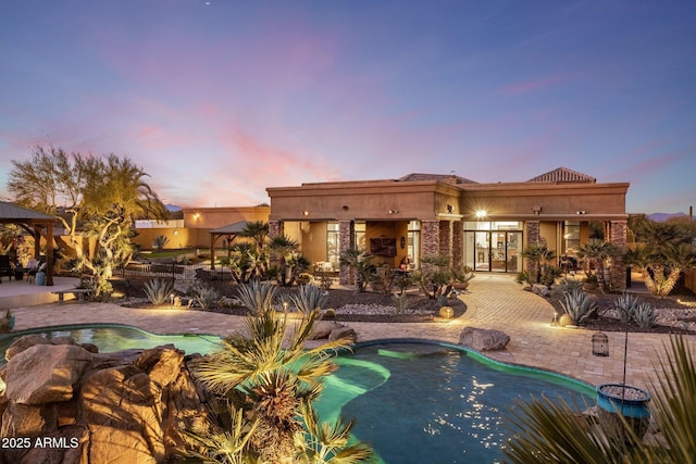 pool at dusk with a fireplace and a patio