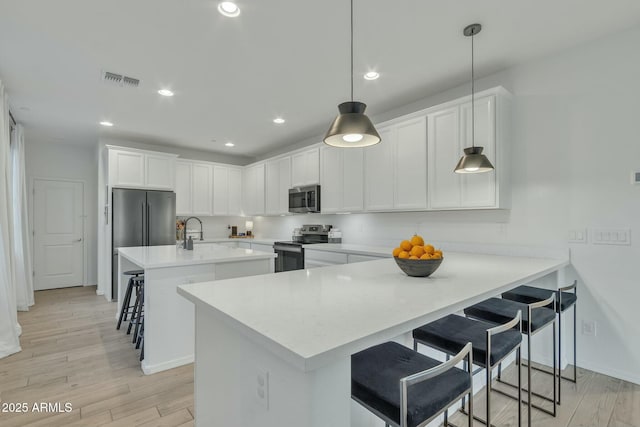 kitchen featuring a kitchen breakfast bar, pendant lighting, white cabinets, light wood-type flooring, and stainless steel appliances