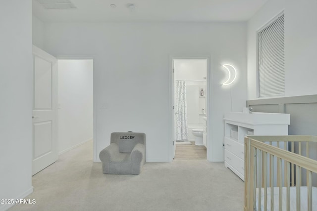 carpeted bedroom featuring a crib and ensuite bath