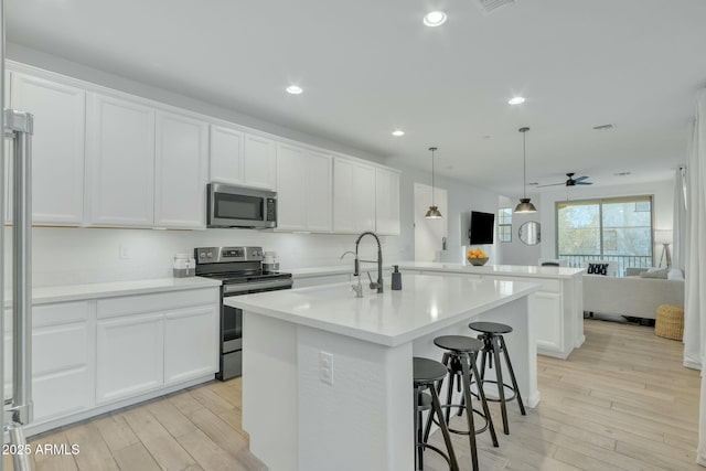 kitchen featuring stainless steel appliances, white cabinetry, a kitchen island with sink, and decorative light fixtures