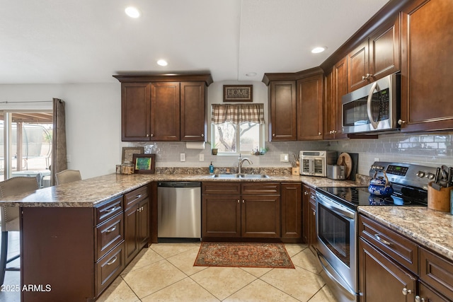 kitchen featuring kitchen peninsula, a kitchen bar, stainless steel appliances, sink, and light tile patterned floors