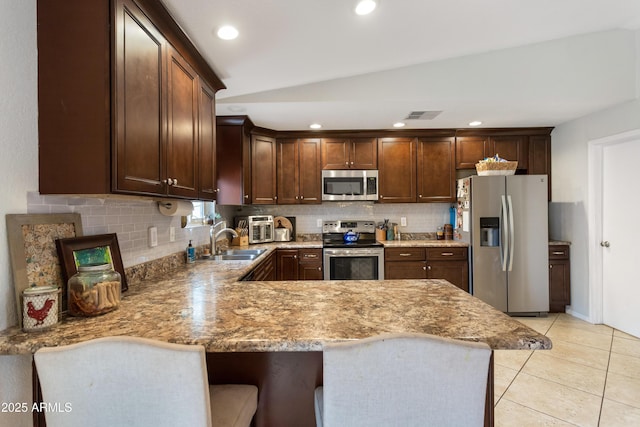 kitchen with a breakfast bar, sink, light tile patterned floors, appliances with stainless steel finishes, and kitchen peninsula