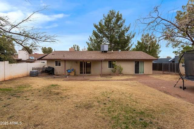 rear view of house with a patio, a trampoline, and a lawn