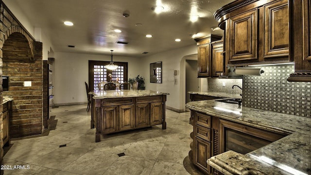 kitchen featuring light stone counters, a center island, pendant lighting, dark brown cabinets, and backsplash