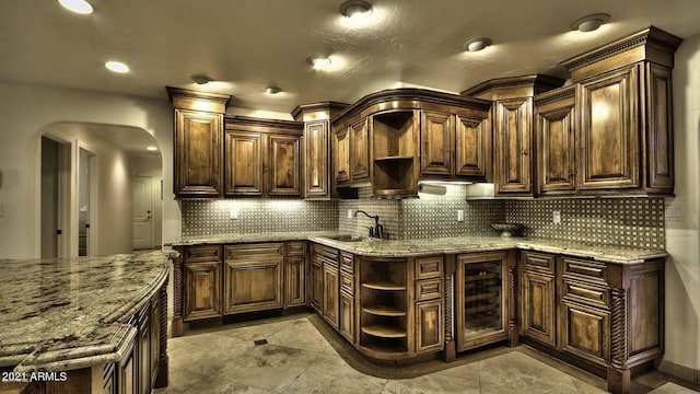 kitchen with dark brown cabinets, light stone counters, decorative backsplash, and sink