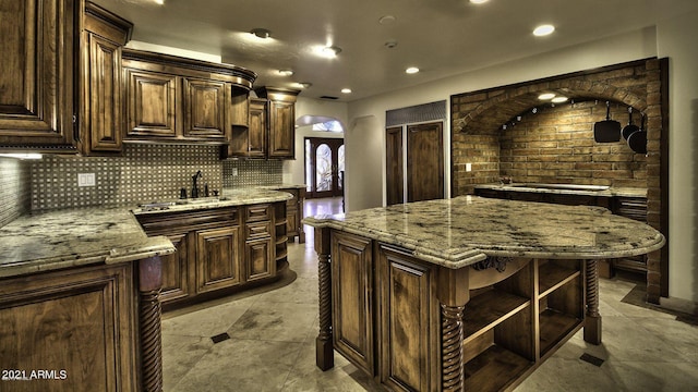 kitchen with light stone countertops, dark brown cabinetry, a center island, tasteful backsplash, and sink