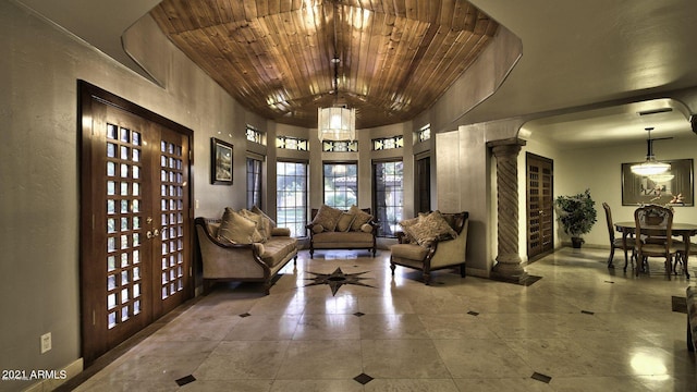 interior space with french doors, a notable chandelier, wood ceiling, and decorative columns