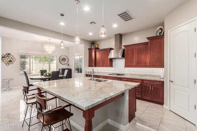 kitchen with sink, a breakfast bar, wall chimney exhaust hood, hanging light fixtures, and stainless steel gas stovetop