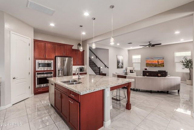 kitchen featuring a center island with sink, appliances with stainless steel finishes, decorative light fixtures, light stone countertops, and sink