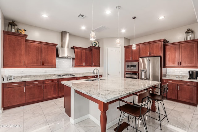 kitchen with stainless steel appliances, sink, a breakfast bar, an island with sink, and wall chimney range hood