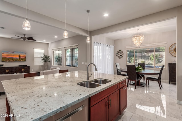 kitchen featuring hanging light fixtures, light stone countertops, sink, and an island with sink