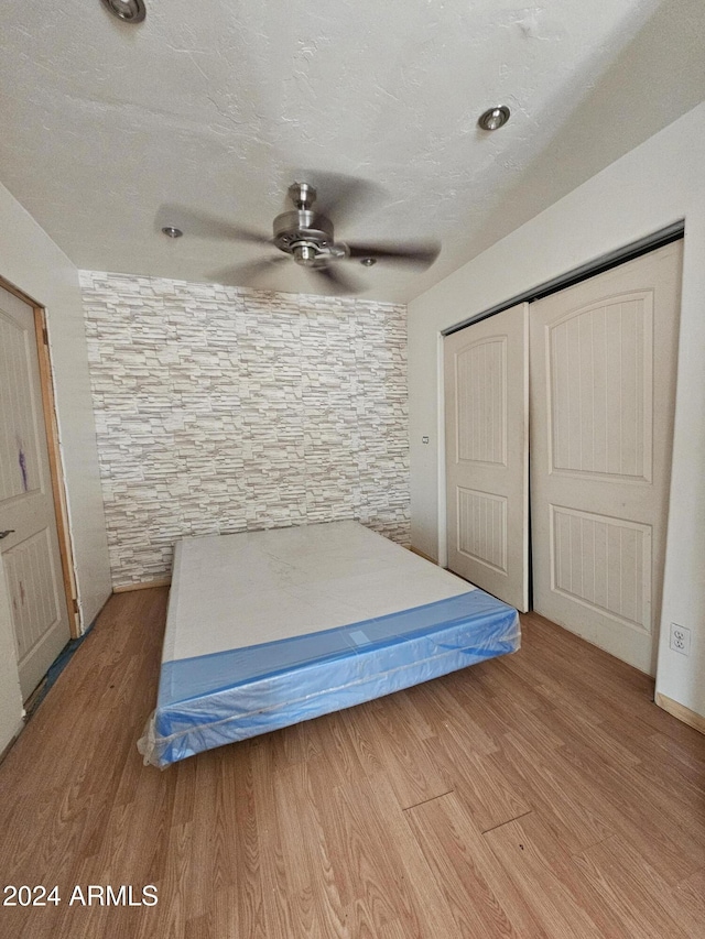 unfurnished bedroom featuring a textured ceiling, light wood-type flooring, a closet, and ceiling fan