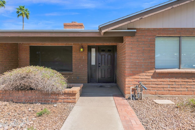 entrance to property featuring a chimney and brick siding