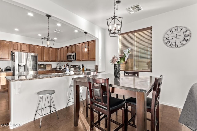 kitchen with pendant lighting, a breakfast bar, dark stone countertops, stainless steel appliances, and dark tile patterned flooring