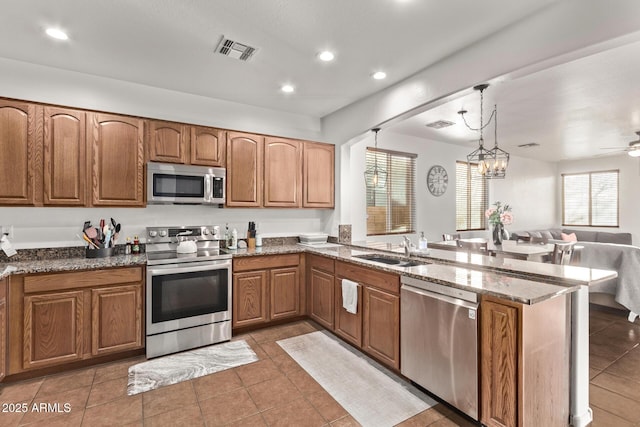 kitchen featuring sink, appliances with stainless steel finishes, dark tile patterned flooring, kitchen peninsula, and pendant lighting