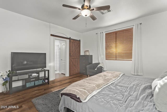 bedroom featuring dark hardwood / wood-style floors, ceiling fan, and a barn door