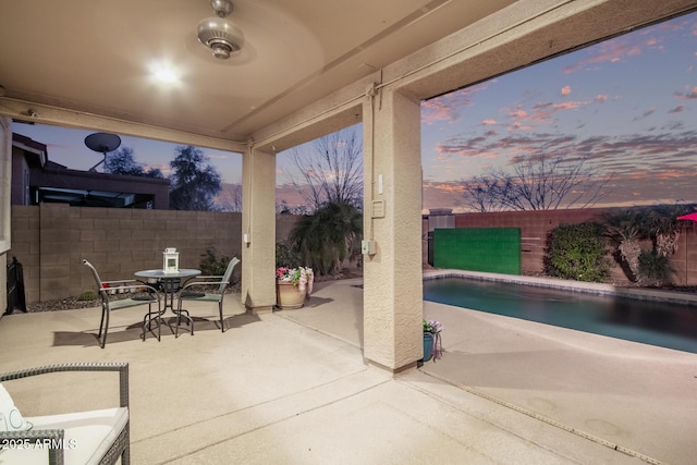 patio terrace at dusk featuring a fenced in pool