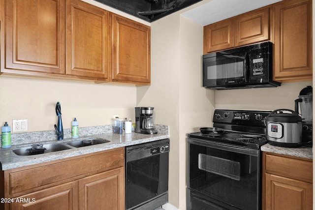 kitchen featuring black appliances, light stone counters, and sink