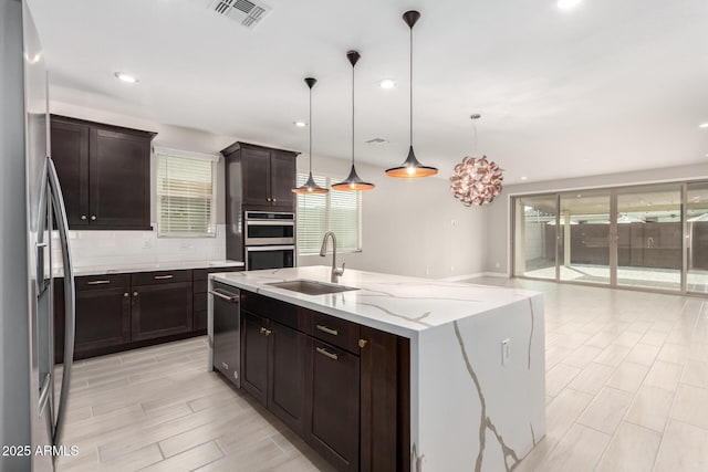 kitchen with sink, hanging light fixtures, stainless steel appliances, a wealth of natural light, and an island with sink