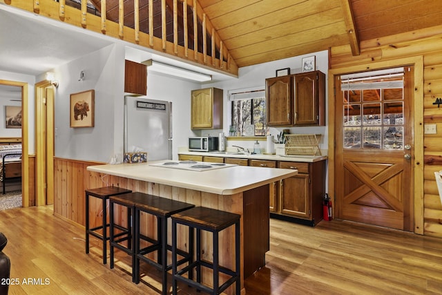 kitchen with appliances with stainless steel finishes, wood walls, a kitchen breakfast bar, light hardwood / wood-style floors, and wooden ceiling