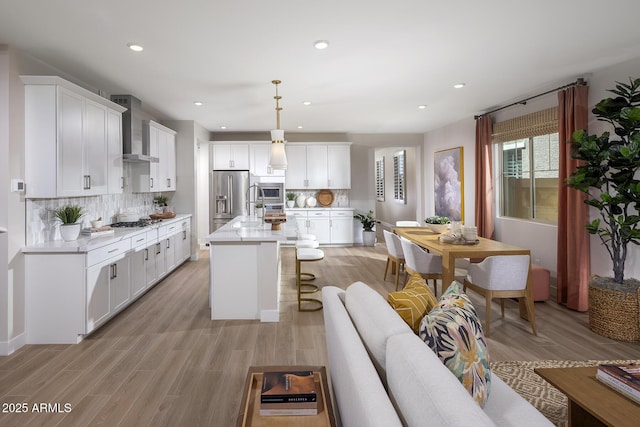 kitchen with white cabinets, hanging light fixtures, appliances with stainless steel finishes, a center island, and wall chimney exhaust hood