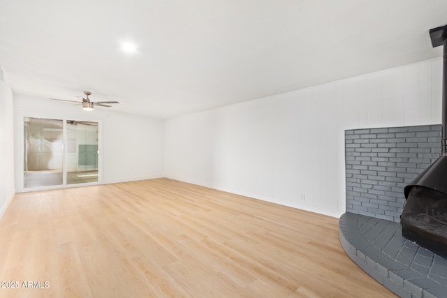 unfurnished living room with a wood stove, ceiling fan, and light hardwood / wood-style flooring