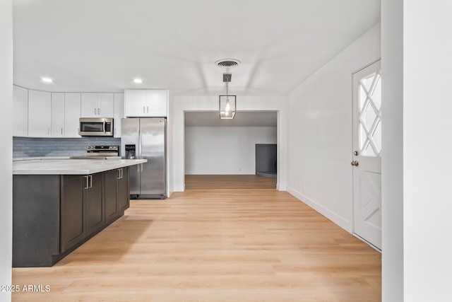 kitchen with stainless steel appliances, backsplash, light hardwood / wood-style floors, decorative light fixtures, and white cabinets