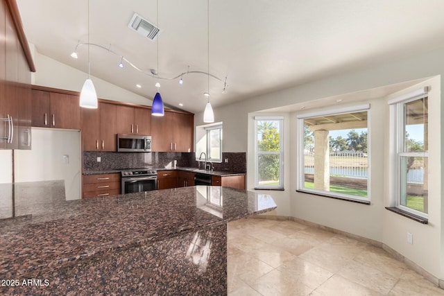 kitchen with lofted ceiling, sink, appliances with stainless steel finishes, hanging light fixtures, and dark stone counters